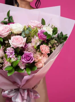 A bouquet of purple and light pink roses wrapped in pink paper
