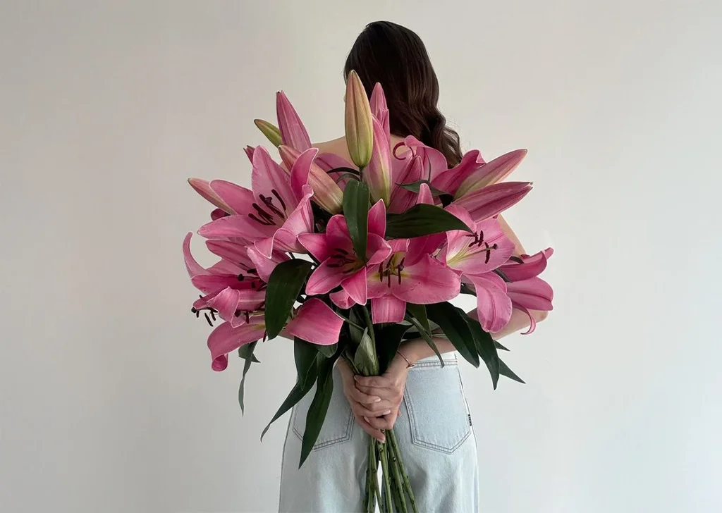 A woman holding a bouquet of pink lilies.