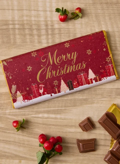 ช็อกโกแลตบาร์เบลเยียม Merry Christmas — ช็อกโกแลตนมห่อด้วยฟอยล์สีทองพร้อมปลอกสีแดงเทศกาล ผลิตด้วยมือโดยช่างช็อกโกแลตจาก UrbanFlowers