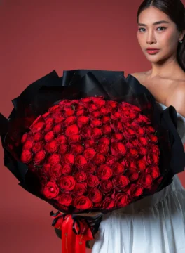 A bouquet of 100 roses wrapped in black paper and compared to the person holding it.